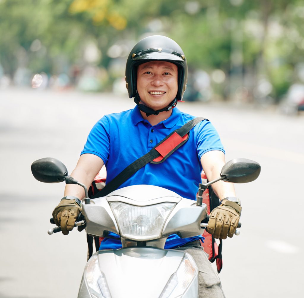 Smiling Asian delivery man riding scooter in the city and delivering products